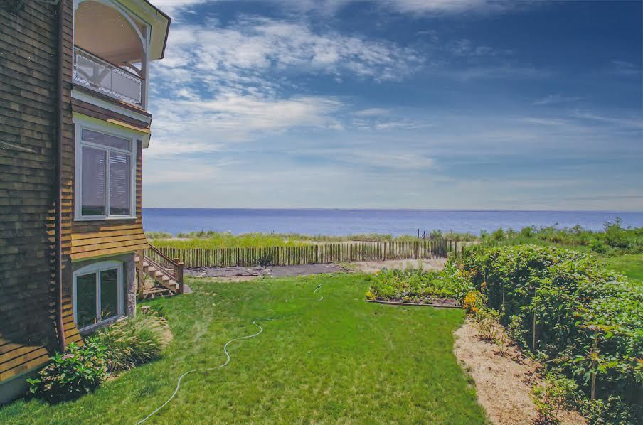 Coastal house with green lawn overlooking the ocean, blue sky with clouds.