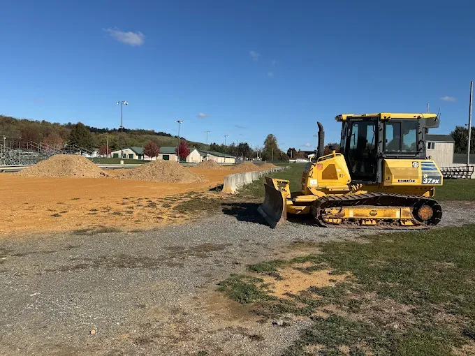 Yellow bulldozer on a dirt lot under a clear blue sky, pushing soil near a road construction site.