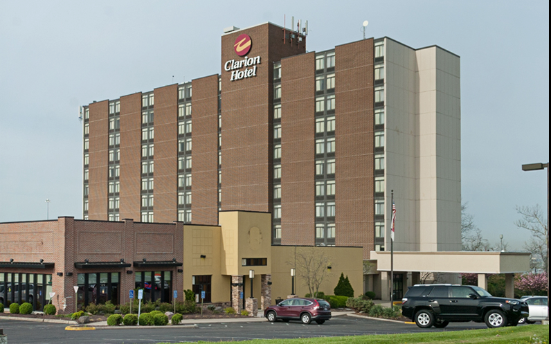 Exterior of a multi-story hotel building with parked cars and a cloudy sky