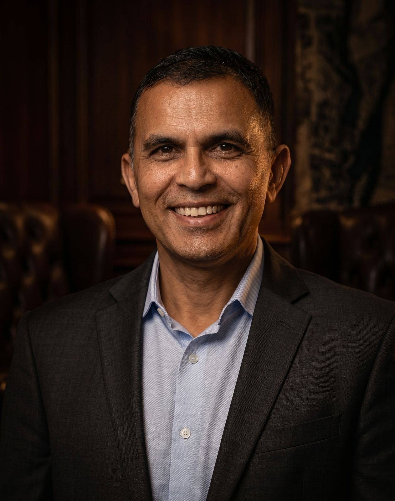 Portrait of a man in a dark blazer and light blue shirt against a white background