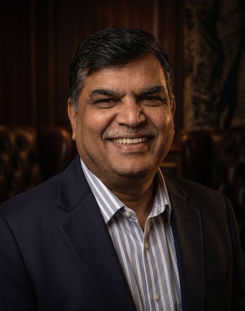 Head-and-shoulders portrait of a man in a dark blazer and striped shirt against a white background