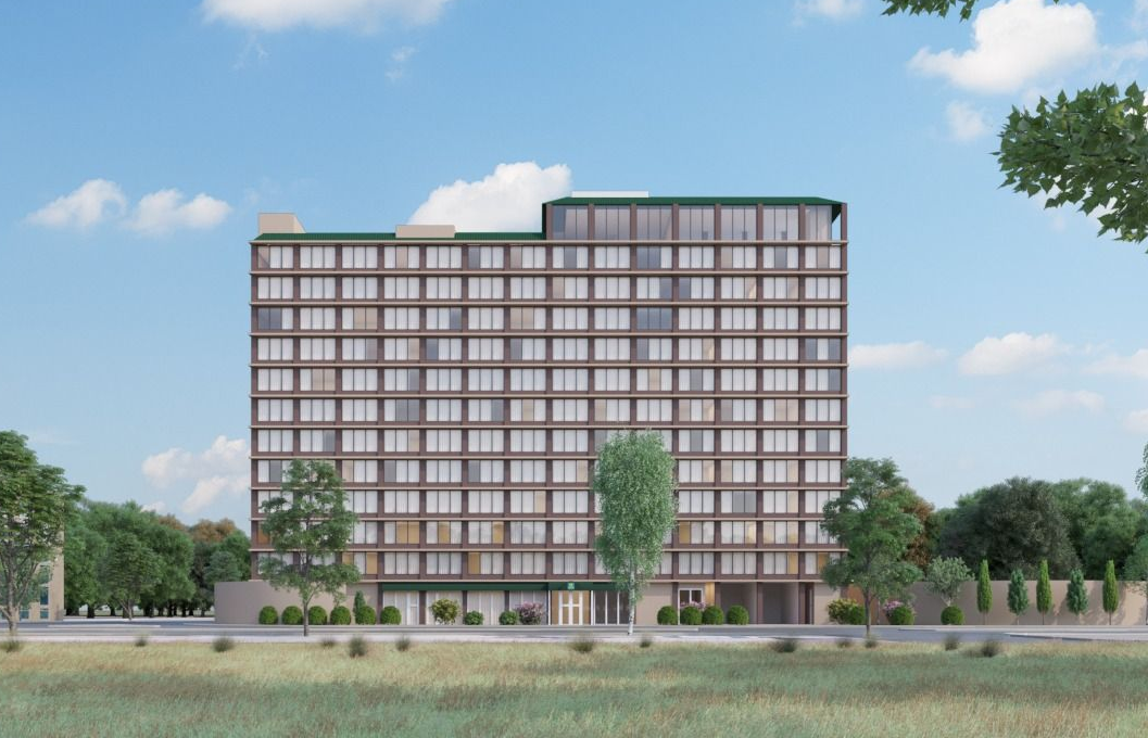 Modern multi-story apartment building with a grid of windows under a blue sky, seen across a grassy foreground