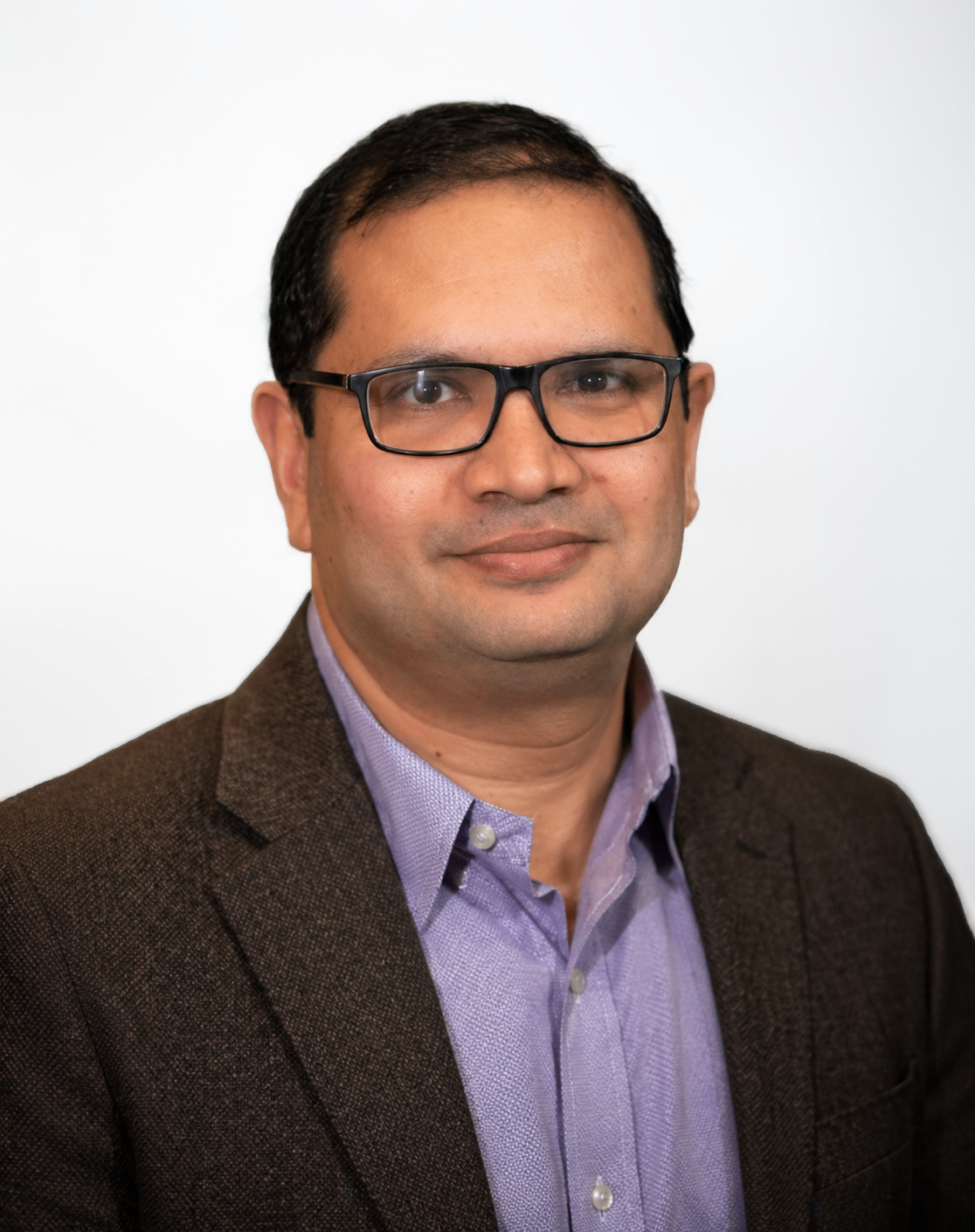 Studio headshot of a person wearing glasses, a purple shirt, and a dark blazer on a light background