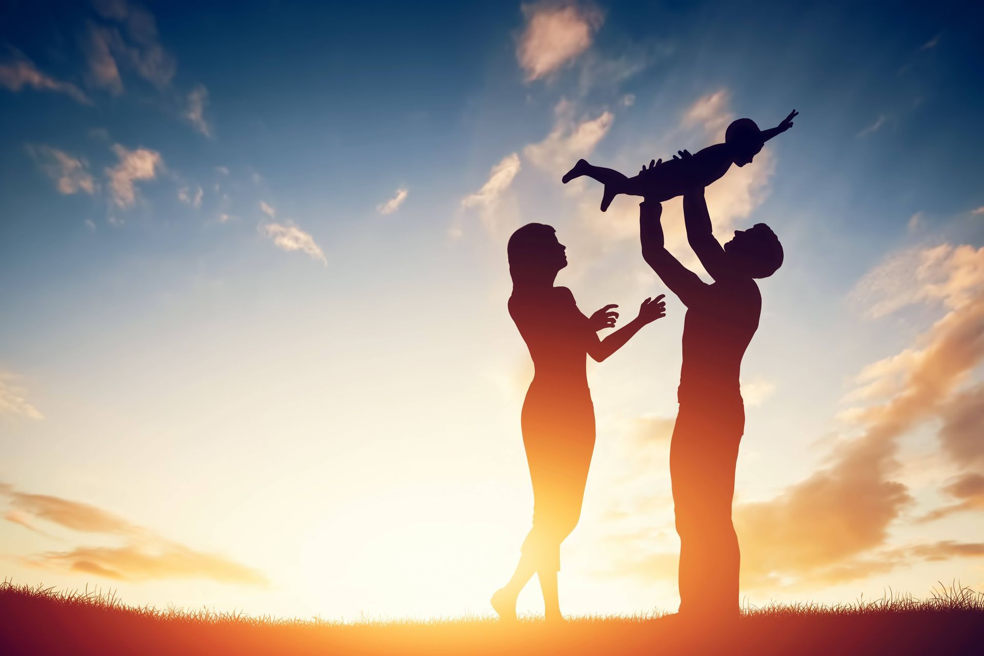 Parents raising their child in their arms at sunset