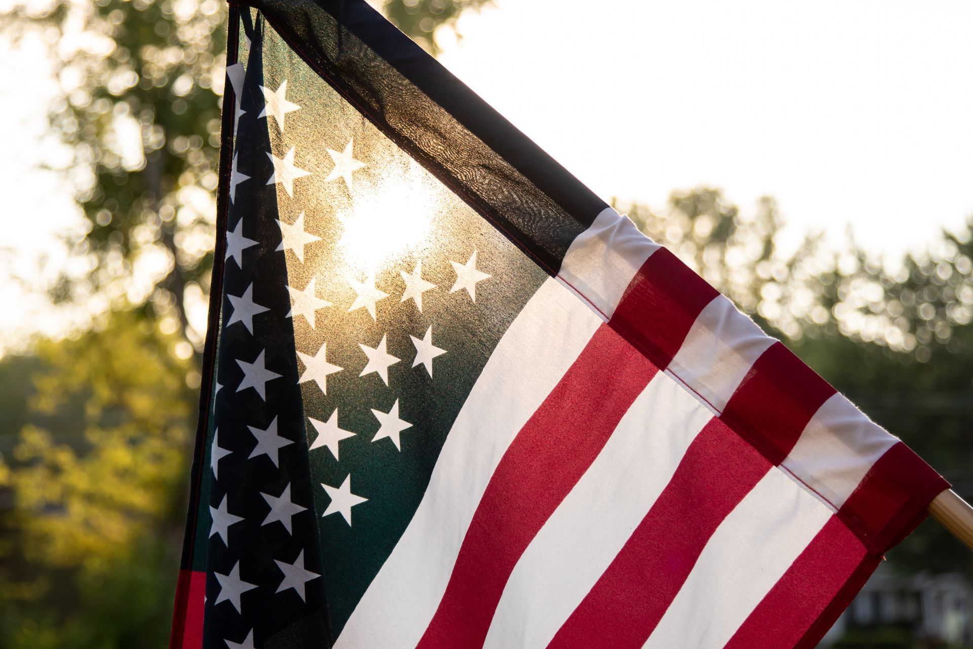 sun peaking through trees and the American flag
