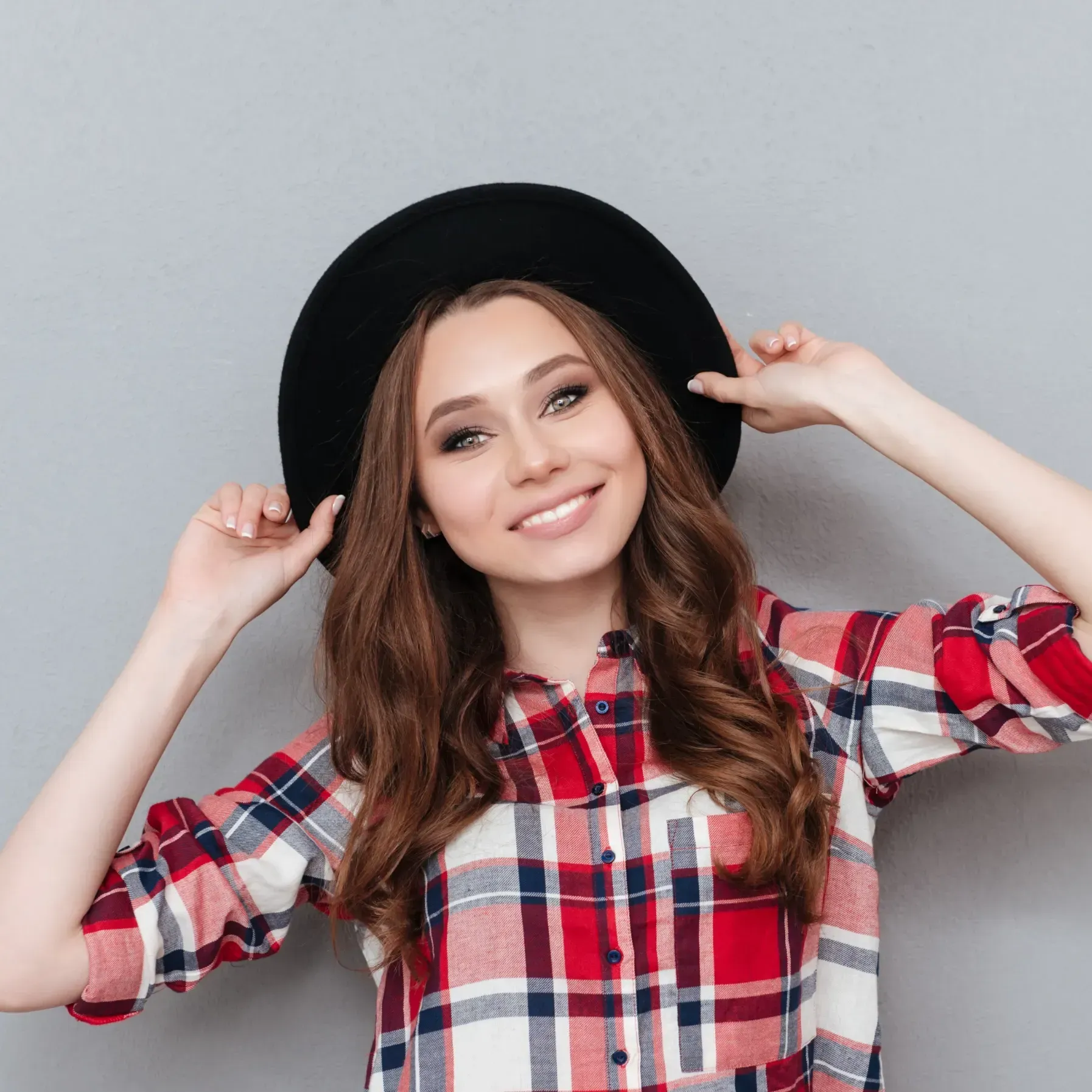 A woman wearing a plaid shirt and a black hat is smiling.