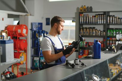 A mechanic is looking under the hood of a car while holding a clipboard.