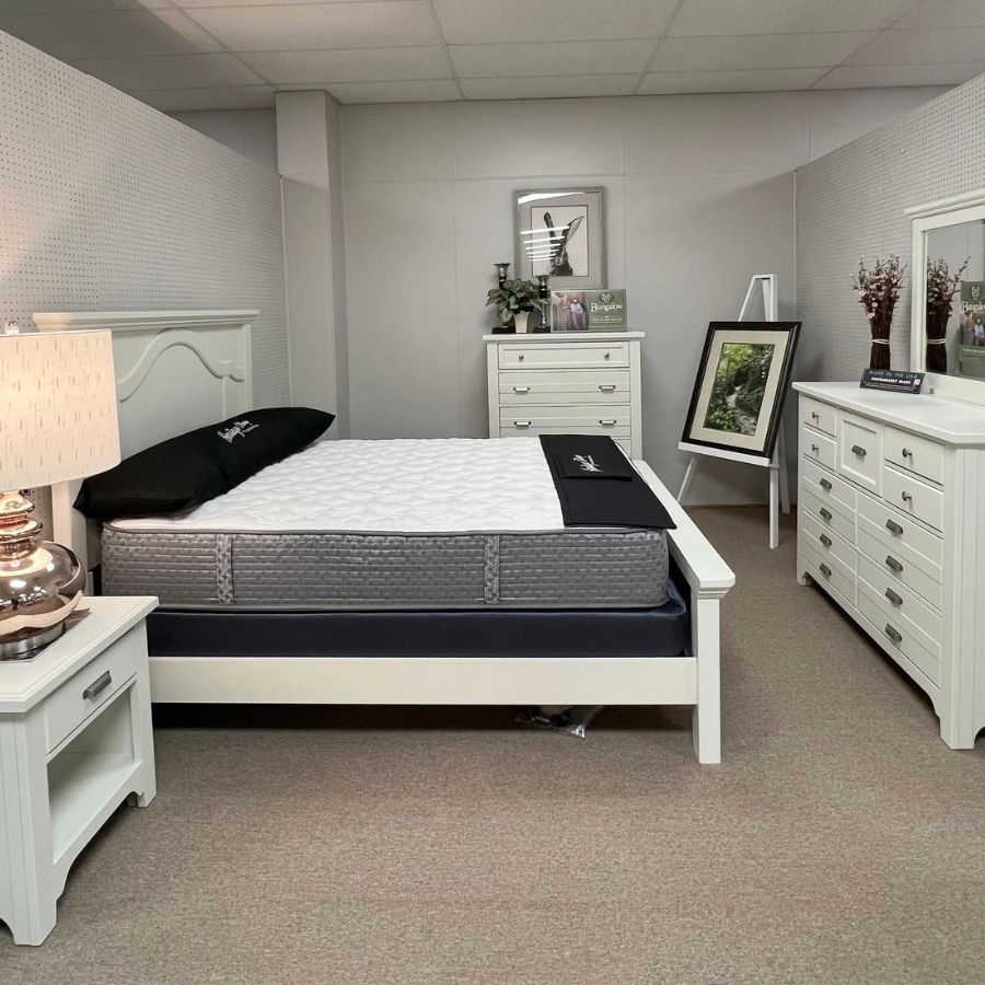 Bright bedroom with white furniture, a made bed, nightstand lamp, and dresser against gray walls.