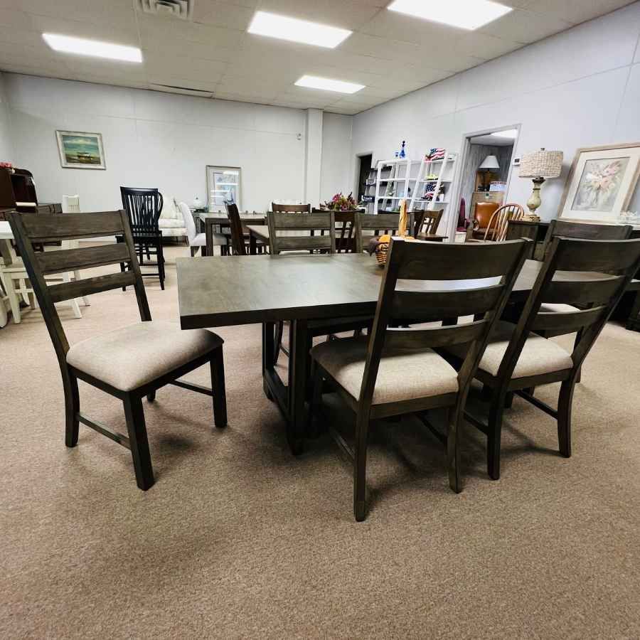 Furniture showroom with a wooden dining table and several chairs on a carpeted floor