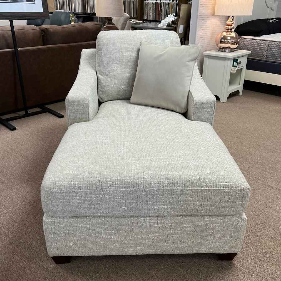 Light gray upholstered chaise lounge chair with matching pillow in a furniture showroom