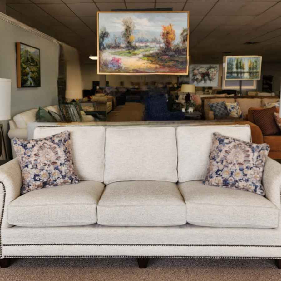White sofa with floral pillows in a furniture showroom, with framed landscape art hanging behind it