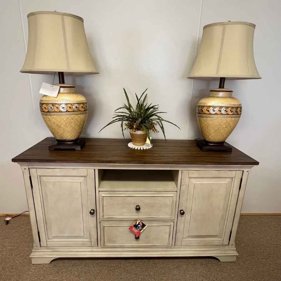 Vintage cream sideboard with dark wood top, two table lamps, and a small plant centered on it.