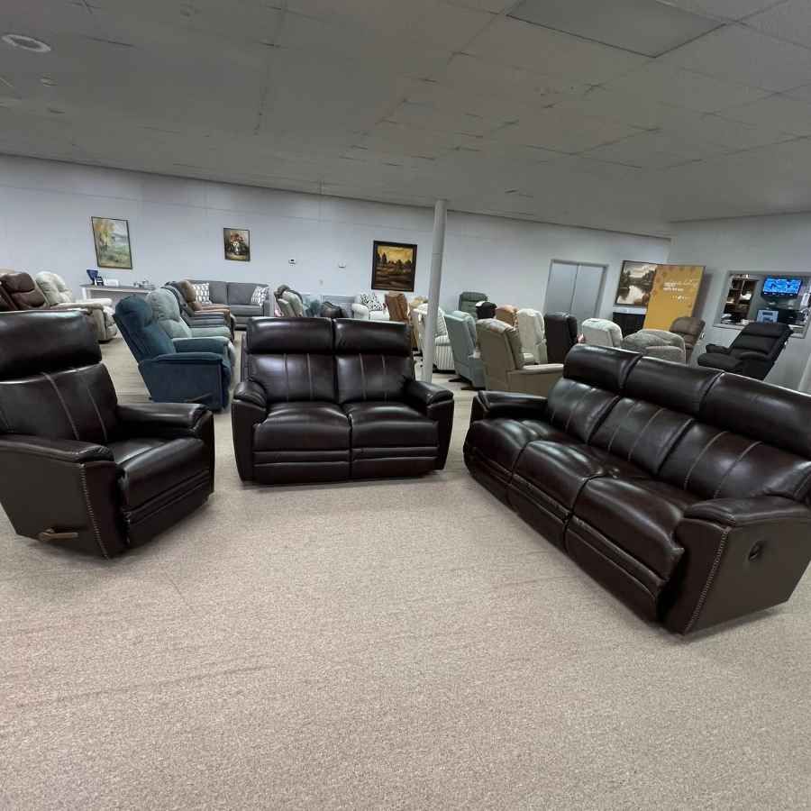 Furniture showroom with dark brown leather sofas and chairs displayed on beige carpet