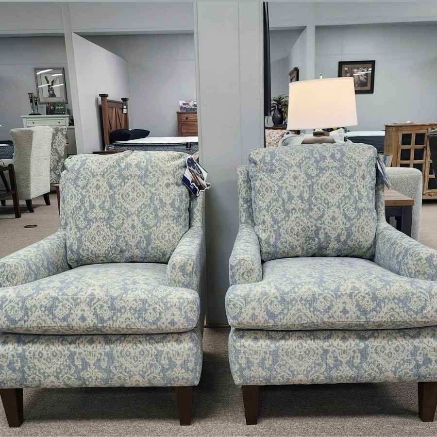 Two cream armchairs in a furniture showroom with lamps and shelves in the background