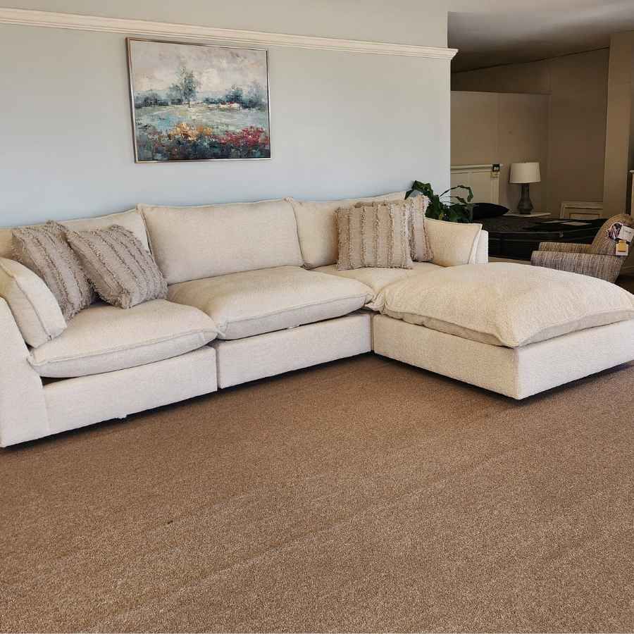 White sectional sofa with beige pillows in a living room with carpet and wall art