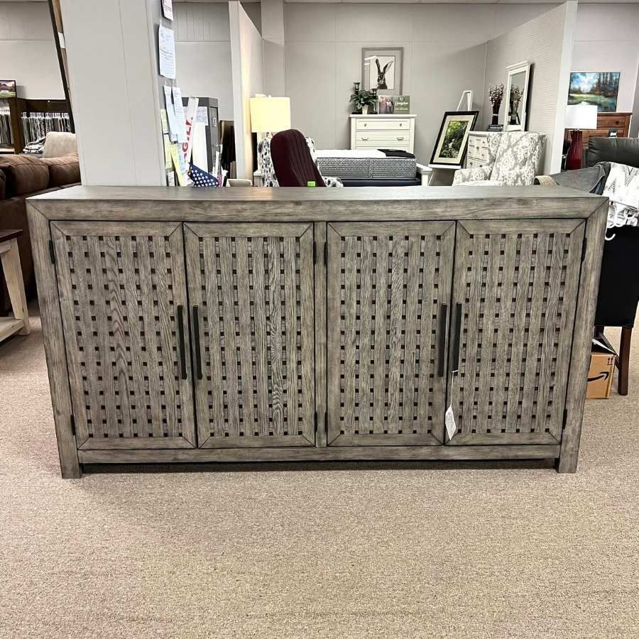 Gray woven-front sideboard in a carpeted showroom, with mirrors and decor on top and behind it