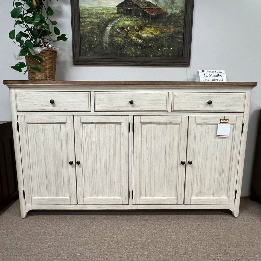 White rustic sideboard cabinet with drawers and doors in a showroom, topped with a plant and framed painting