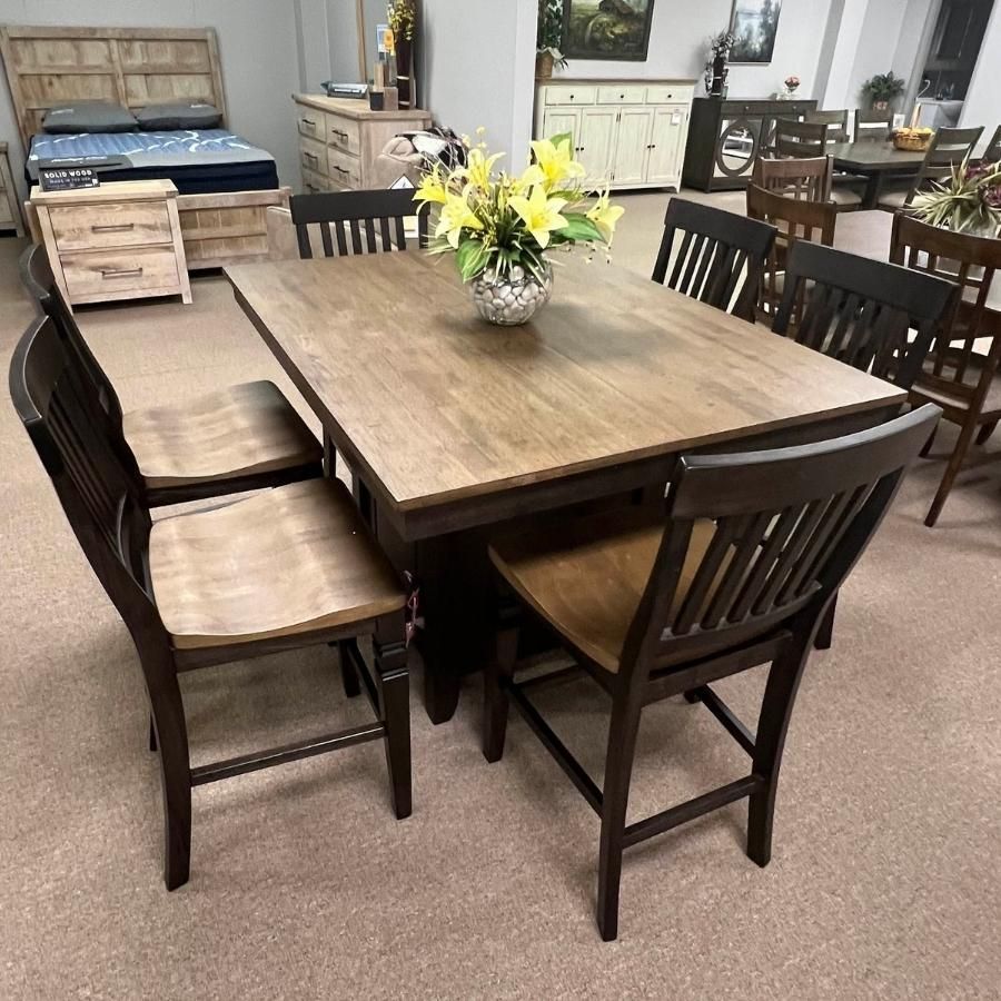 Wooden dining table with six chairs and a yellow flower centerpiece in a room with furniture displays