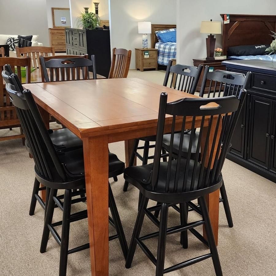 Wooden dining table with four black chairs in a furniture showroom, with bedroom sets in the background