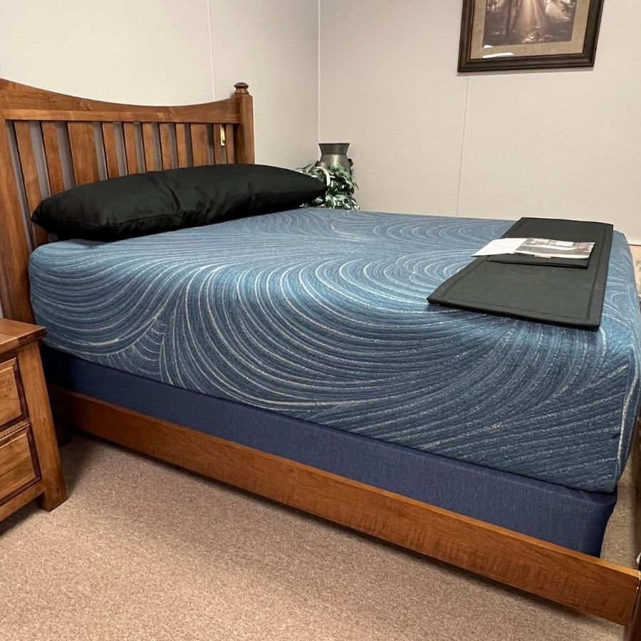 Wooden bed with blue quilt and black pillow in a bedroom, with folded linens at the foot of the bed