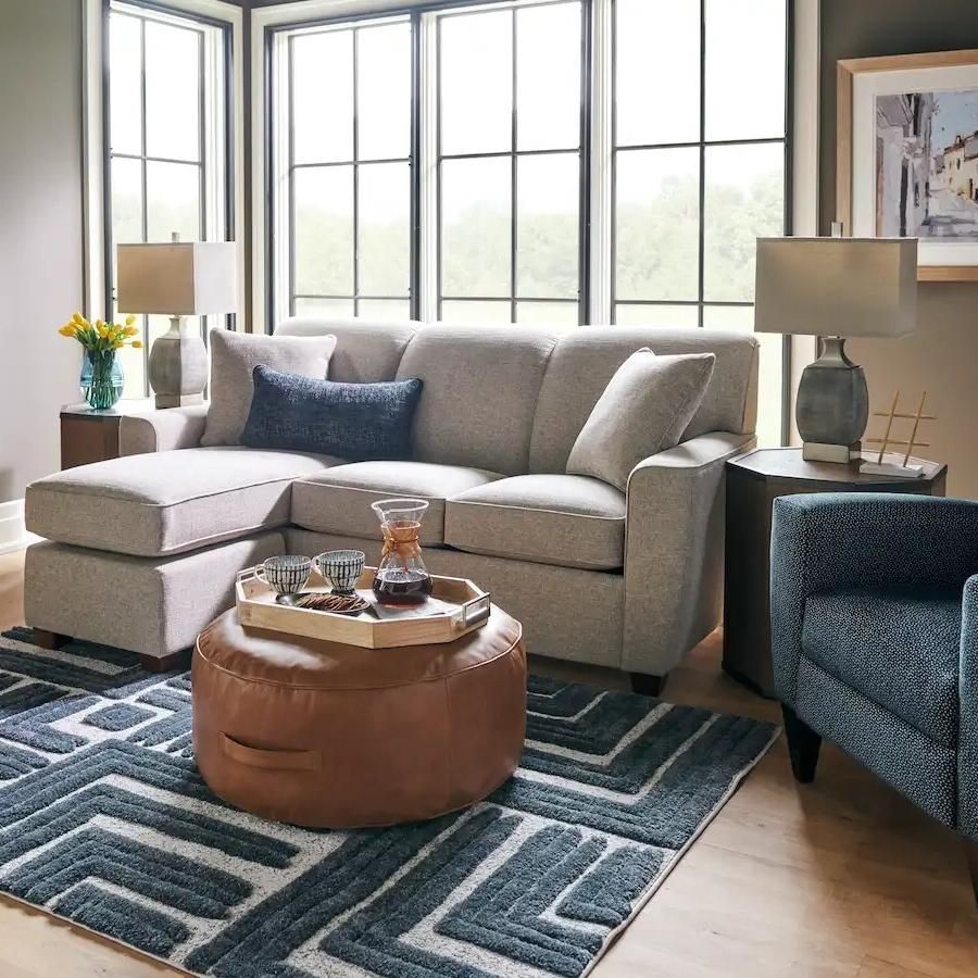 Living room with a gray sofa, blue rug, brown ottoman, and large windows