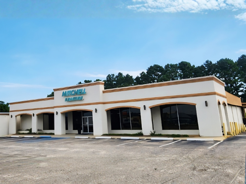 Mitchell Furniture storefront with blue sign, white building, and parked car on a sunny street