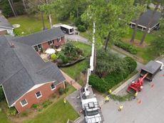 Crane lifts a utility pole beside brick homes on a residential street, with workers and cones nearby