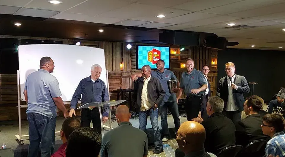 A group of men are standing in front of a group of people in a room.