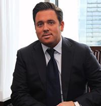 A man in a suit and tie is sitting in a chair in front of a window.