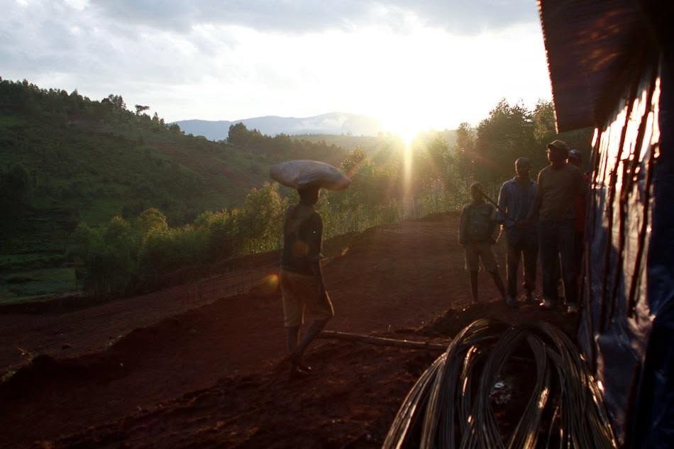 People standing by a roadside at sunset, with a sunlit valley and hills in the background.