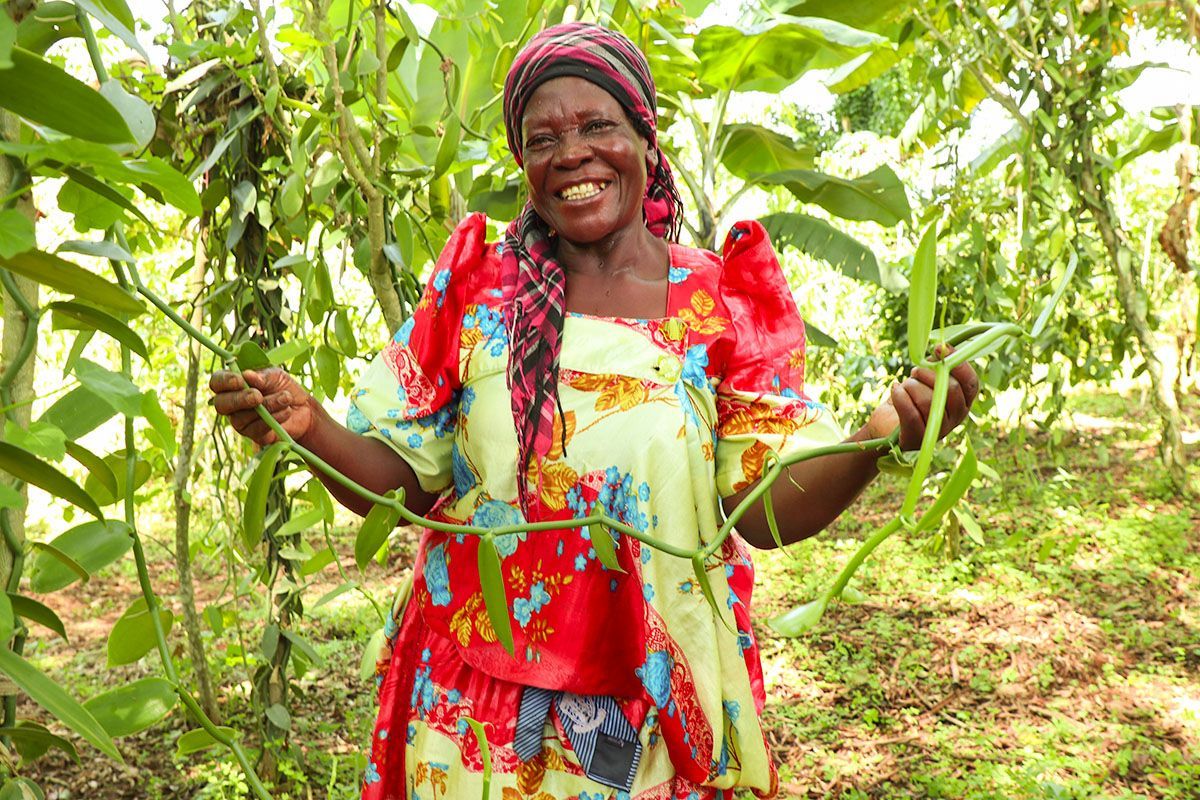 Smiling person in a red floral dress standing among green plants in a garden