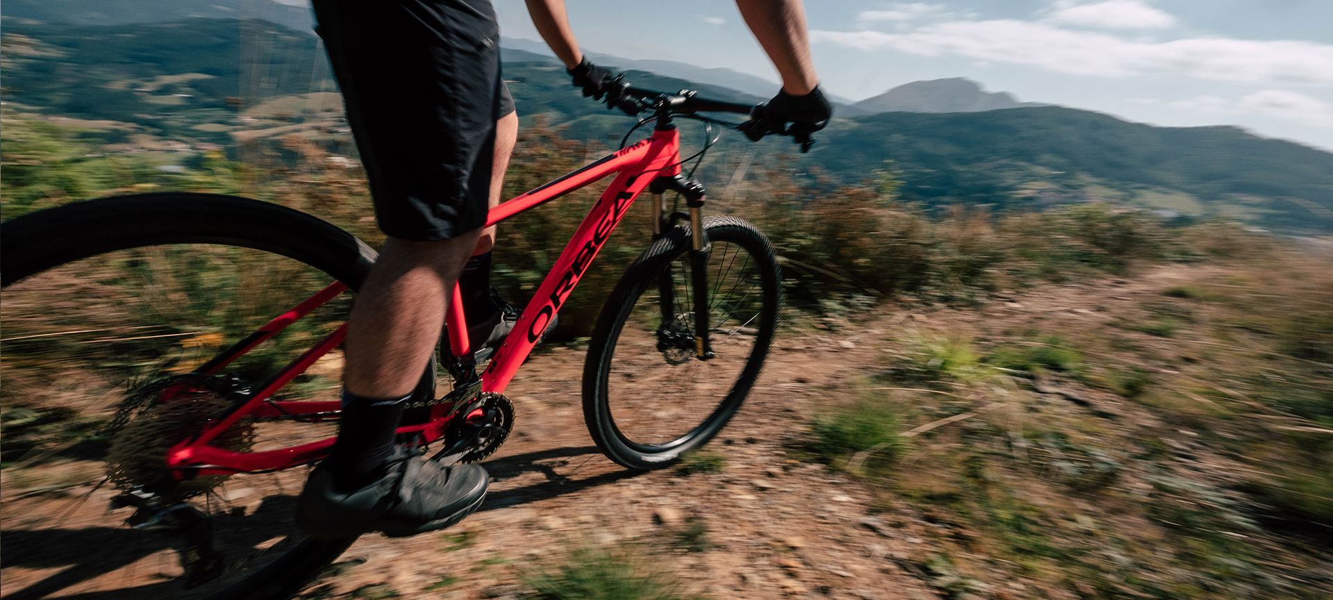 Cyclist in a neon green shirt riding a mountain bike on a wooded trail beside a steep hillside