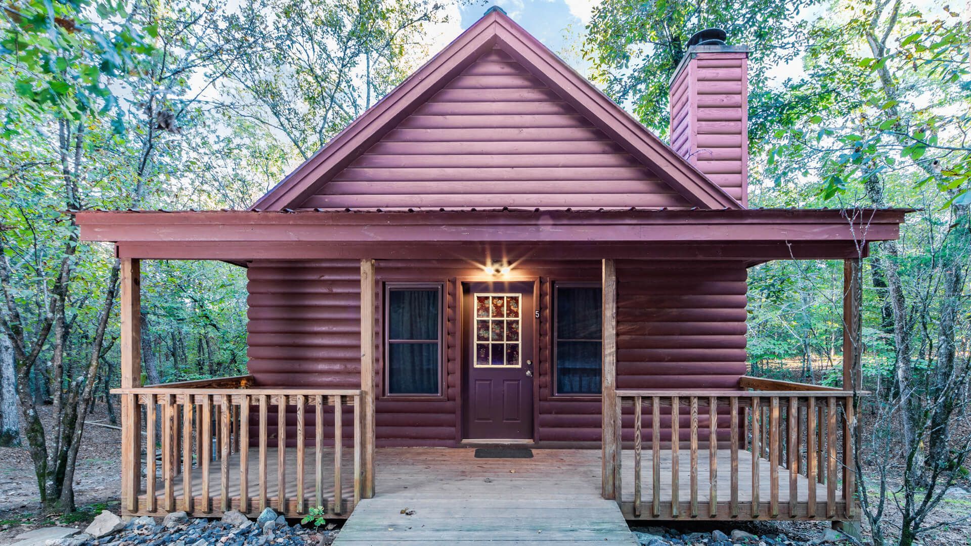 Cozy wooden cabin with a front porch, peaked roof, and lit doorway surrounded by trees.