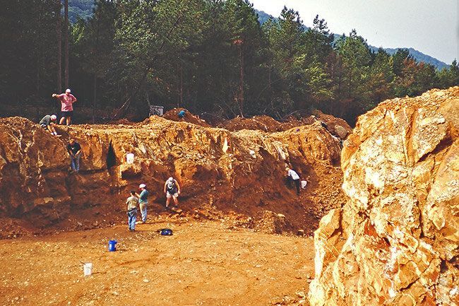 People working at a rocky excavation site with trees in the background