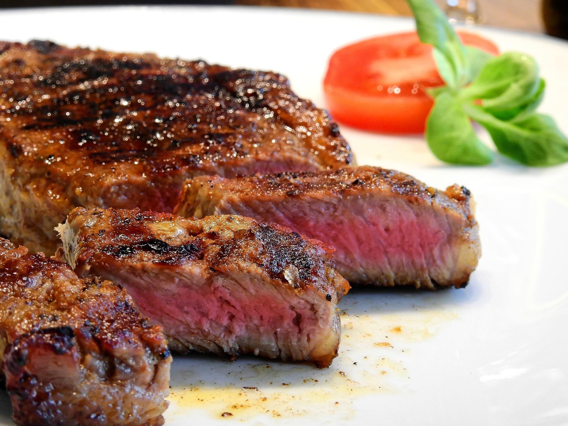 Grilled steak slices on a white plate with tomato and basil garnish