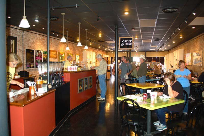 Busy restaurant interior with diners seated at tables and staff behind a red counter.