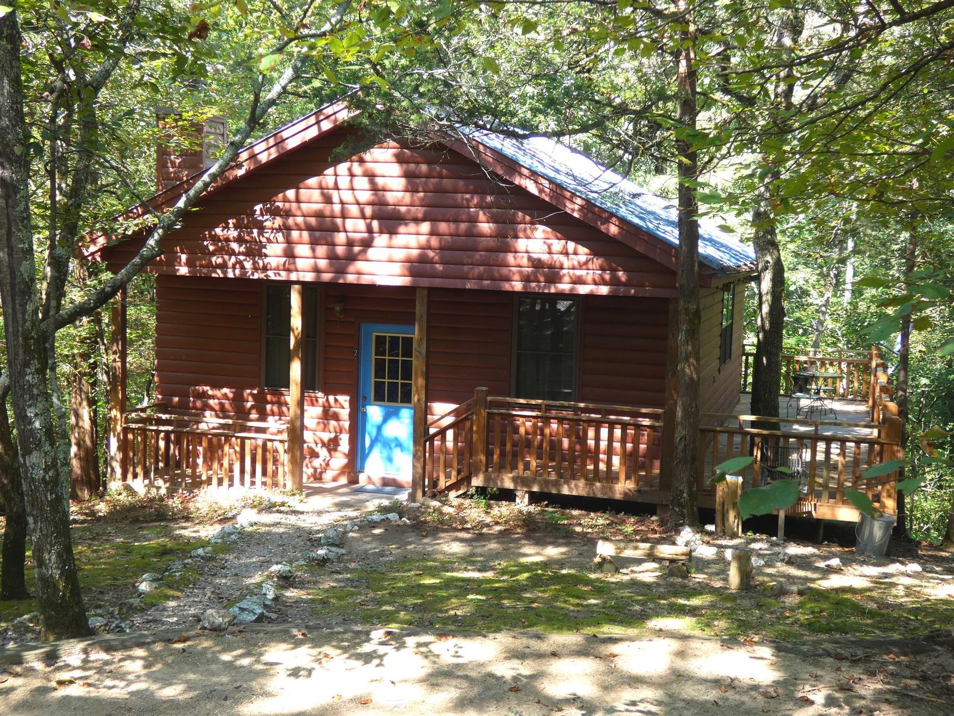 Small red cabin with blue door and porch in a wooded area