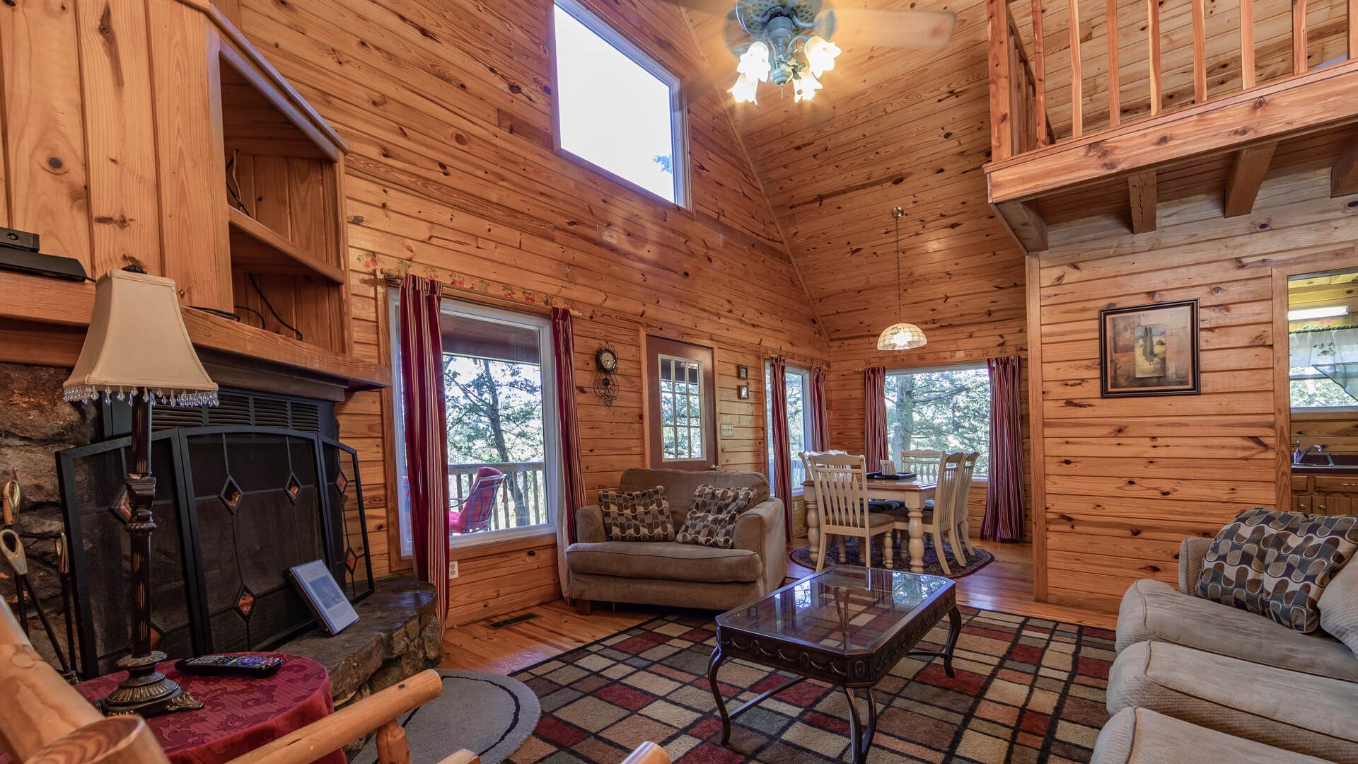Cozy log cabin living room with stone fireplace, plaid rug, and wooden staircase leading to loft