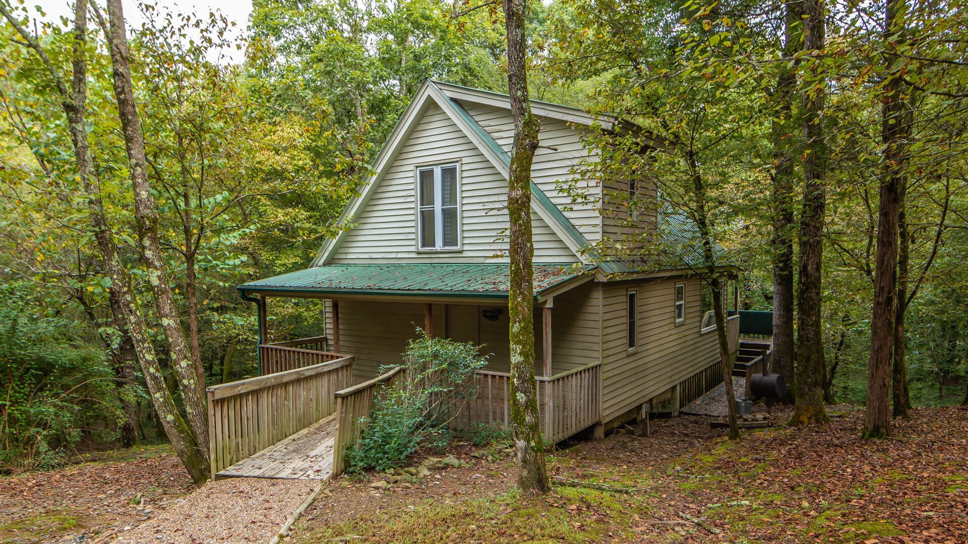 Small gray cabin with green porch roof nestled in a wooded forest setting
