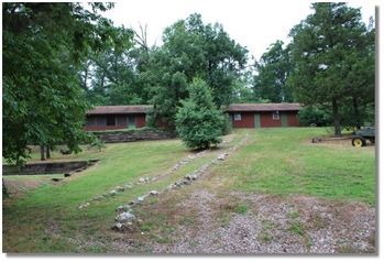 Rustic brick houses amid green lawns and trees, with a rocky drainage path in the foreground