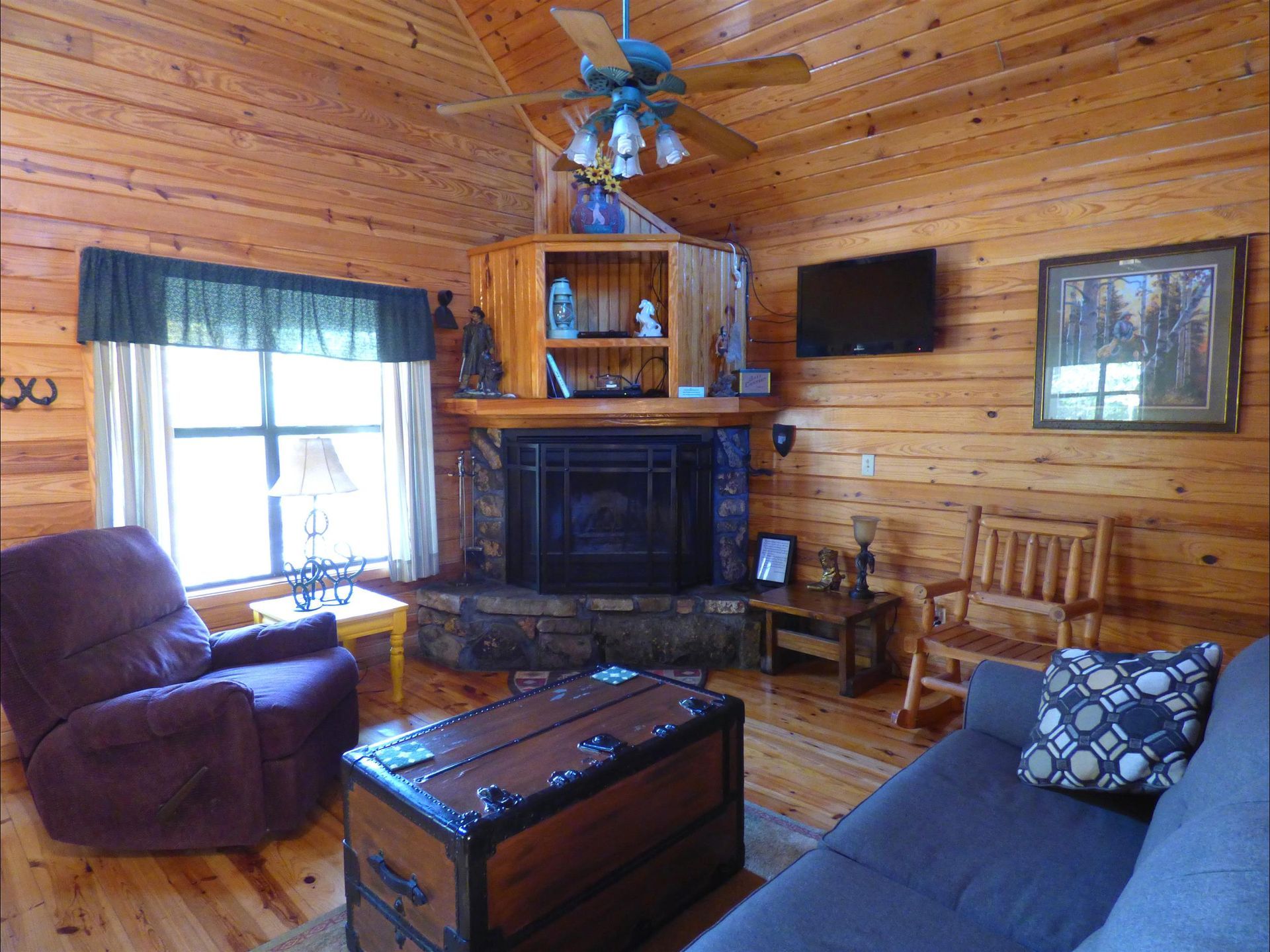 Cozy log cabin living room with fireplace, wood walls, recliner, sofa, and TV.