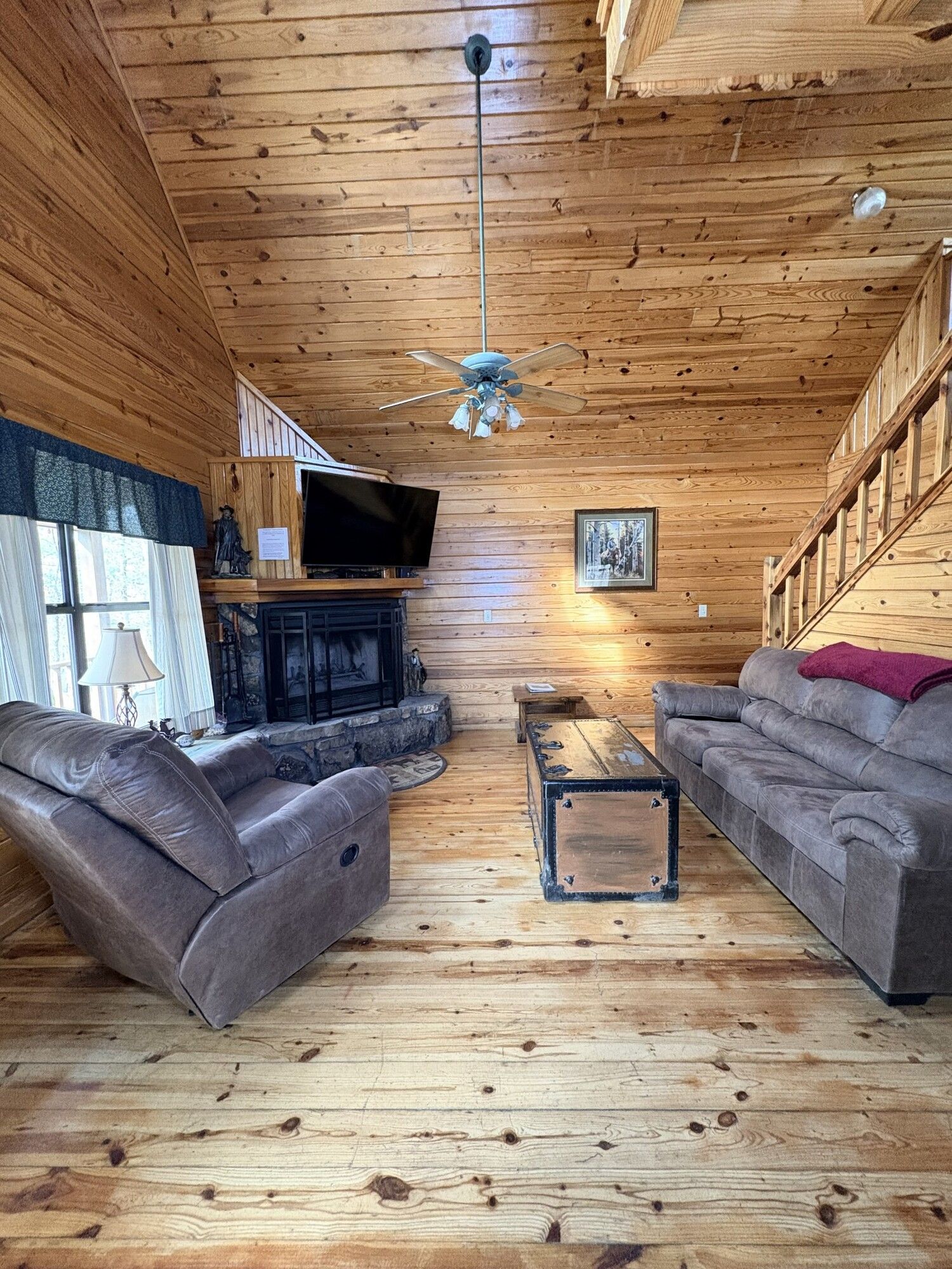 Cozy log cabin living room with leather sofas, stone fireplace, wood walls, and vaulted ceiling