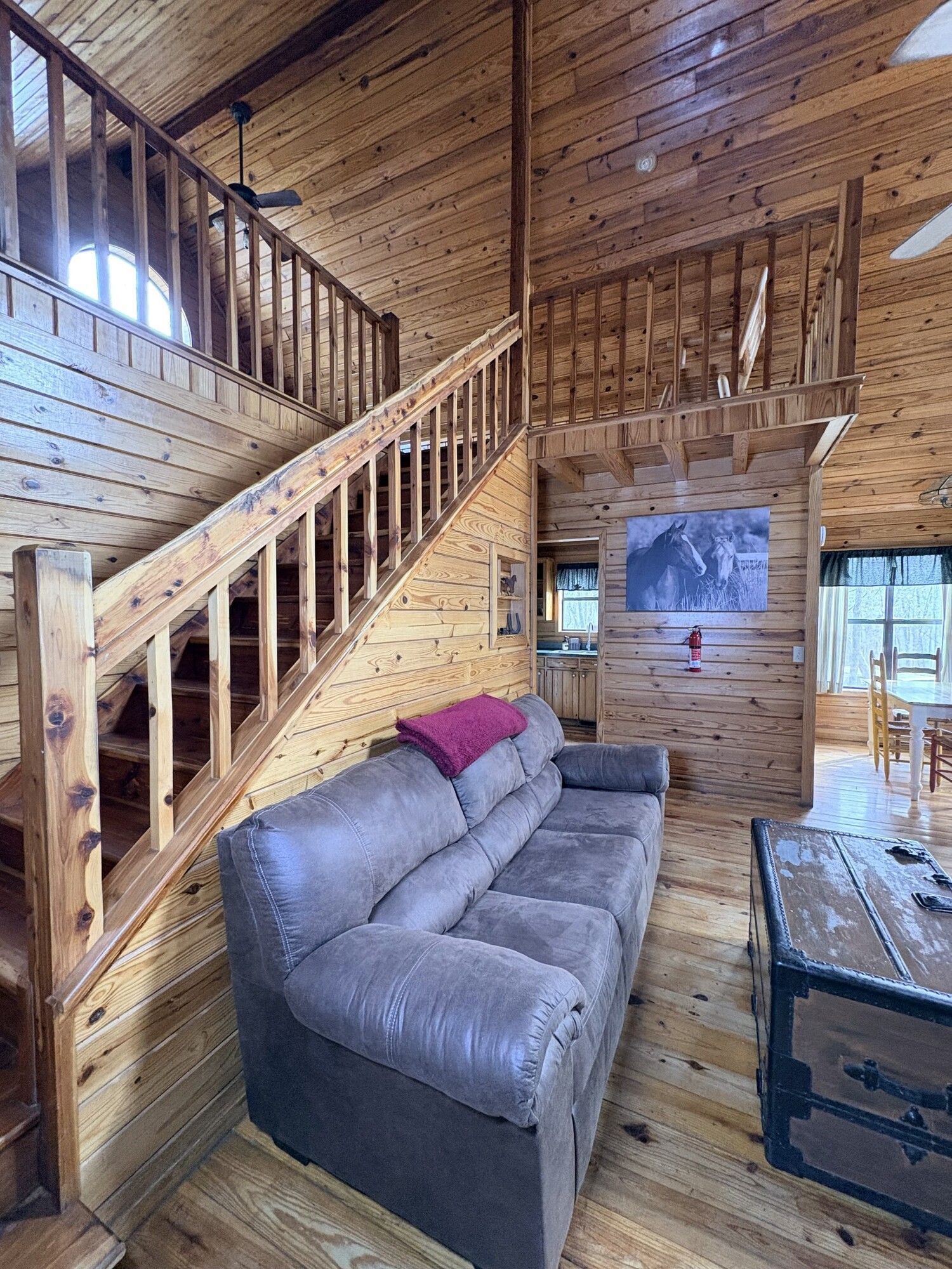 Wood-paneled cabin living room with gray sofa, staircase, and rustic chest table