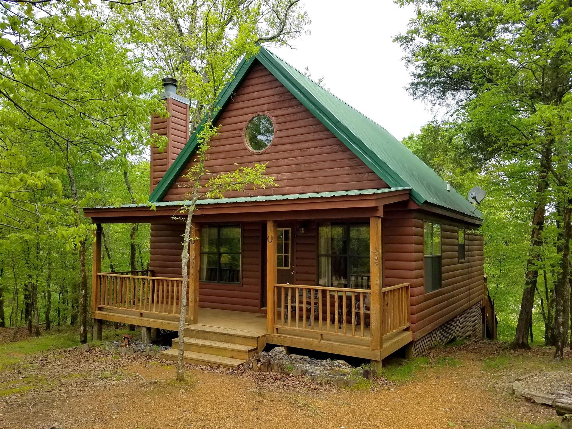 Wooden cabin with green roof and porch in a wooded forest setting