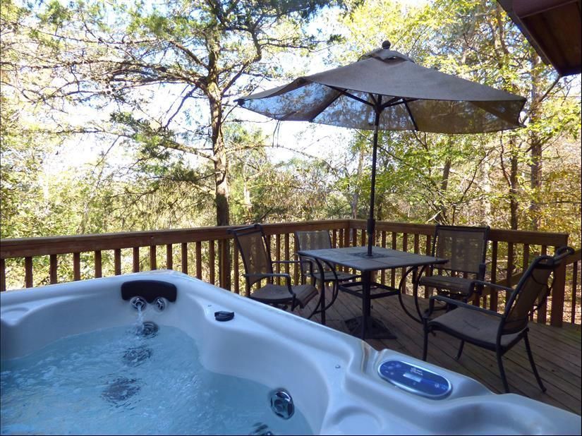 Outdoor deck with hot tub, patio table, and umbrella overlooking trees