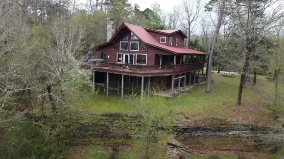 Red house on stilts in a wooded, overgrown clearing near a pond