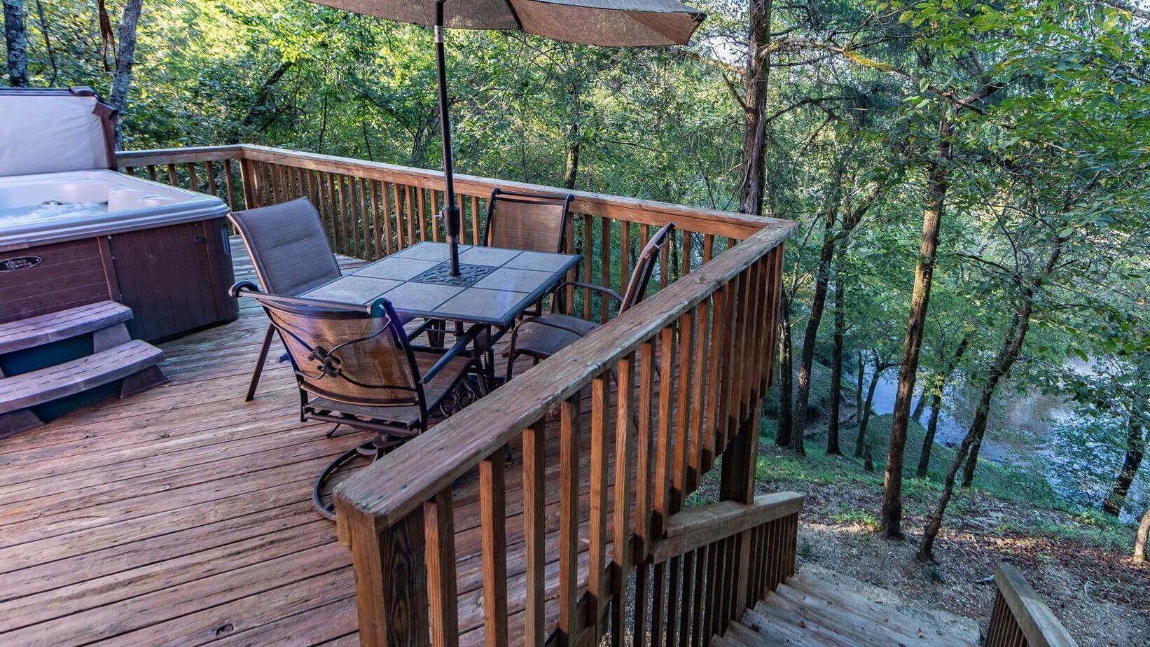 Wooden deck with patio table, chairs, umbrella, and hot tub overlooking a wooded hillside