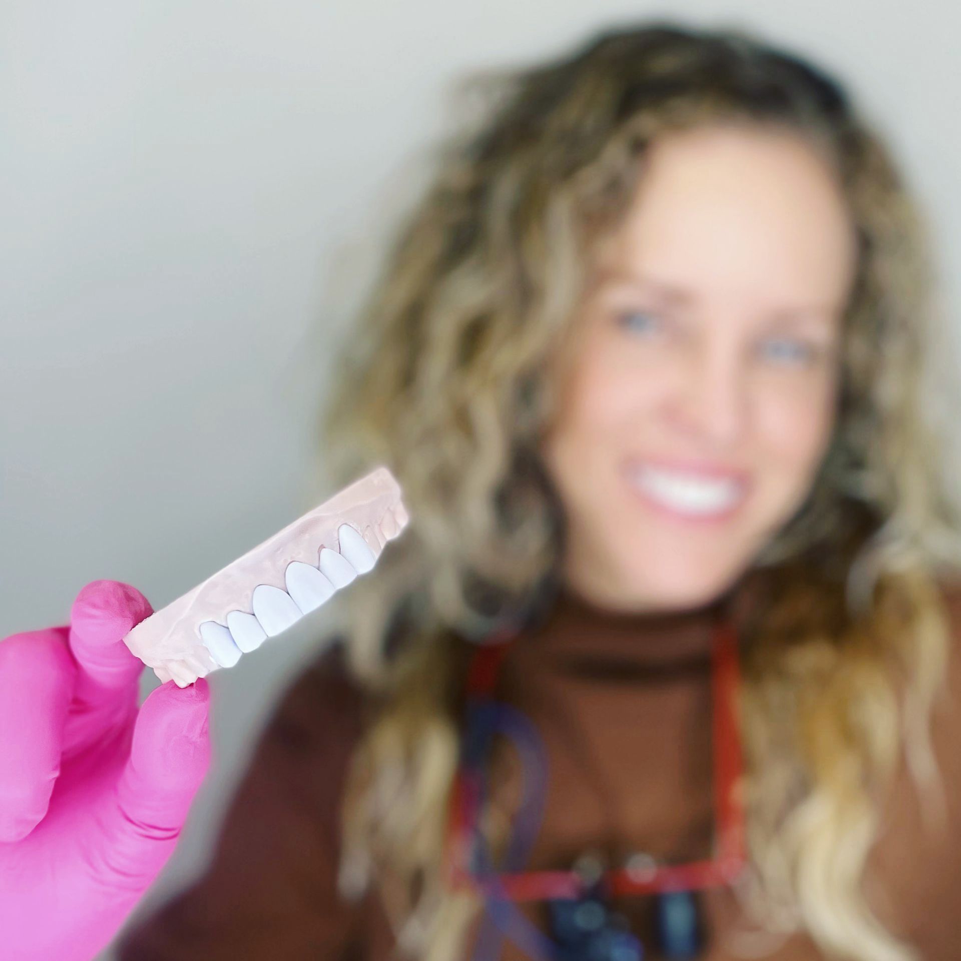 Pink-gloved hand holding a clear dental aligner in front of a smiling person
