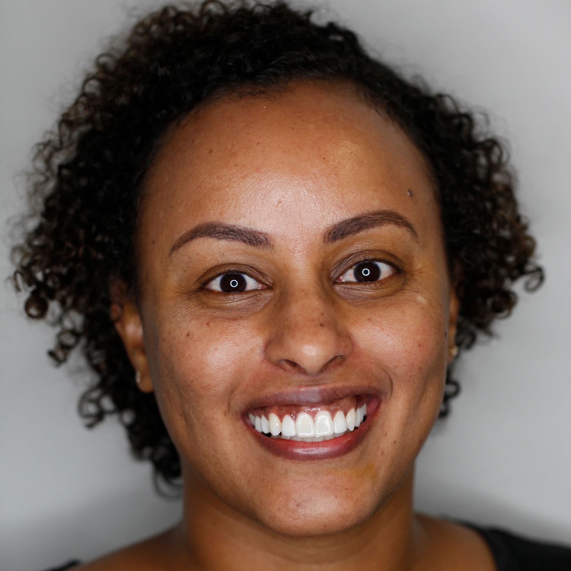 Smiling person with curly hair against a gray background