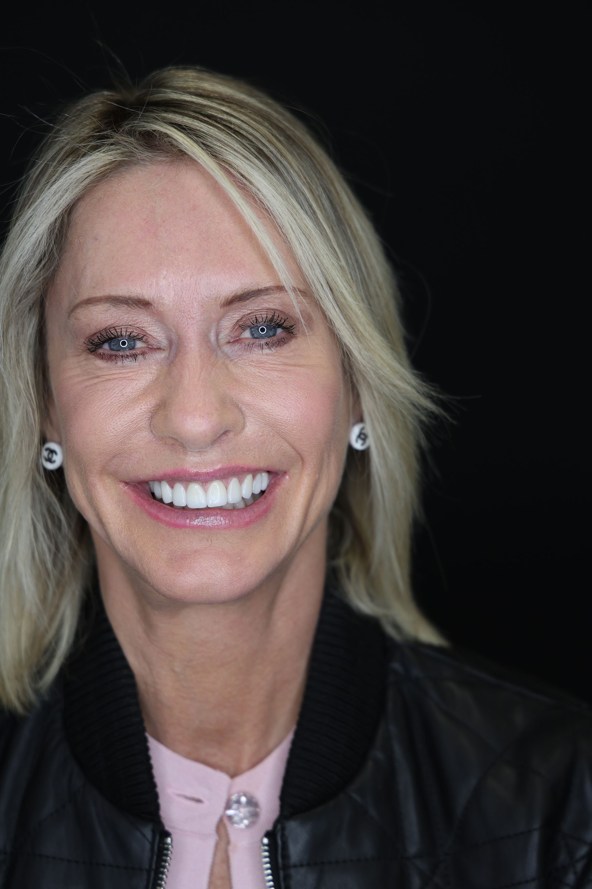 Smiling blonde woman in a black jacket against a dark background